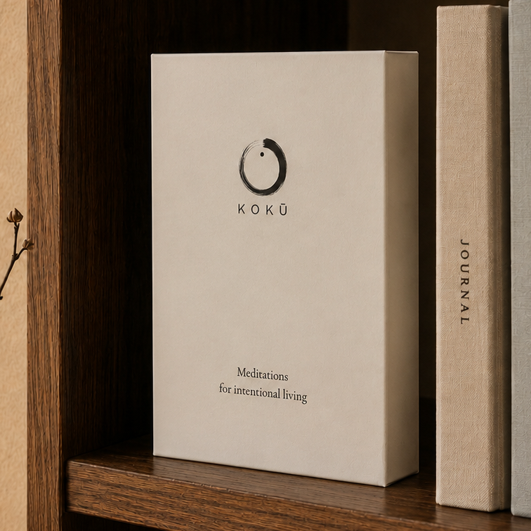 A white Koku book style box standing on a wooden shelf beside several books, with warm natural light and a vase in the background.